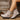 Beige ankle boots with black soles worn by a person against a wooden background