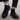 Black Chelsea boots worn with rolled-up jeans on a textured surface