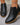 Black ankle boots with brown soles on a gray floor