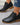 Black ankle boots with brown soles worn by a person on a gray surface