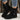 Black suede boots worn with rolled-up jeans against a rustic wooden background