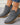 Gray ankle boots with brown soles worn by a person on a light gray floor
