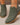 Green ankle boots with brown soles worn by a person on a neutral background