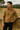 Man wearing a brown sweater standing against a stone wall with a natural landscape in the background