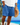 Man wearing blue drawstring shorts with pockets, holding a straw hat on the beach in casual summer outfit
