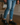 Man wearing light blue ripped jeans and black leather Derby shoes with yellow stitching, standing on a dark wooden floor in a stylish indoor setting