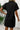 Person wearing a black dress with a white wall and plant in the background