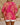 Person wearing a bright pink and yellow patterned top with white shorts on a beige background