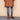 Person wearing a brown coat, gray pants, and brown shoes on a beige background