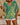 Person wearing a green and yellow patterned top with white shorts indoors