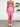 Pink strapless dress with a high slit worn by a person, standing against a white wall with a plant in the corner