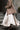 Woman in a beige coat and white dress walking up steps