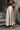 Woman in a stylish outfit with a long beige coat, satin skirt, and brown top standing on steps