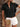 Woman wearing a black ruffled blouse with white shorts, holding a beige clutch