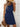 Woman wearing a blue dress with a straw hat and brown handbag against a light background