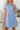 Woman wearing a blue dress with a textured pattern, holding a straw bag indoors