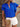 Woman wearing a blue ruffled blouse with white shorts, holding a brown clutch