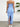 Woman wearing a blue strapless dress with a slit, standing against a white wall with a plant in the corner
