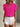 Woman wearing a bright pink blouse with ruffled sleeves and white shorts against a neutral background