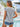 Woman wearing a floral top and denim shorts by a poolside with palm trees in the background