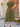 Woman wearing a green dress standing outdoors near a wooden door and wicker chair