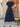 Woman wearing a navy blue dress standing outdoors near a wooden door and wicker chair