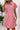 Woman wearing a pink dress with a textured pattern, holding a phone and a clutch, against a light background