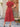 Woman wearing a red dress standing outdoors near a wooden door and wicker chair