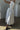 Woman wearing a white dress with a high neckline and flowing skirt in a minimalistic setting