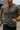 A fit Australian man in his 30s wearing a dark grey short-sleeve Henley shirt, captured mid-motion outdoors in natural light. The setting is casual yet premium, with the model exuding confidence and ease