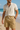 A smiling man in a cream short-sleeve shirt and khaki linen-blend cargo shorts walking on a sunny beach in Australia, hands in pockets, with waves in the background