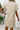 Beige textured dress worn by a person with a white wall and plant in the background