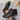 Black ankle boots with brown soles held by a hand on a gray surface
