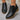 Black ankle boots with brown soles on a gray floor