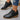 Black ankle boots with brown soles worn by a person on a gray surface
