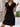 Woman wearing a black dress with a wooden wall and plant in the background