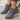 Gray ankle boots with brown soles worn by a person on a light gray floor