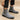 Gray suede Chelsea boots worn with black pants on a beige background