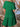Green dress with ruffled details worn by a person, against a wooden background