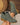 Green suede ankle boots with brown soles held by a hand on a neutral background