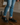 Man wearing light blue ripped jeans and black leather Derby shoes with yellow stitching, standing on a dark wooden floor in a stylish indoor setting