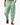 Man wearing loose green drawstring pants with side pockets and sandals while walking on white background