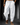 Man wearing loose white drawstring pants with side pockets and sandals while walking on urban pavement