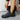 Person putting on a black shoe with a zipper over a gray boot
