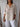 Person wearing a beige shirt and white pants against a wooden paneled wall