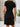 Person wearing a black dress standing against a wooden and white wall with a plant in the background, back view