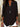 Person wearing a black long-sleeve top with a necklace, standing indoors