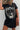 Person wearing a black t-shirt with a graphic design and holding a brown leather bag