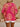 Person wearing a bright pink and yellow patterned top with white shorts on a beige background