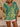 Person wearing a green and yellow patterned top with white shorts indoors
